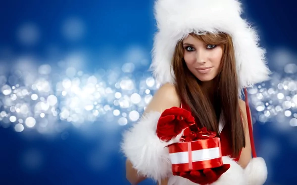 A beautiful woman in a festive white hat and cozy fur outfit holds a red gift, set against a sparkling blue background in this vibrant 4K Ultra HD wallpaper.