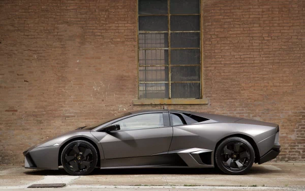 Silver Lamborghini Reventon supercar parked beside a brick wall, captured in a sharp HD desktop wallpaper showcasing the sleek design of this luxury vehicle.