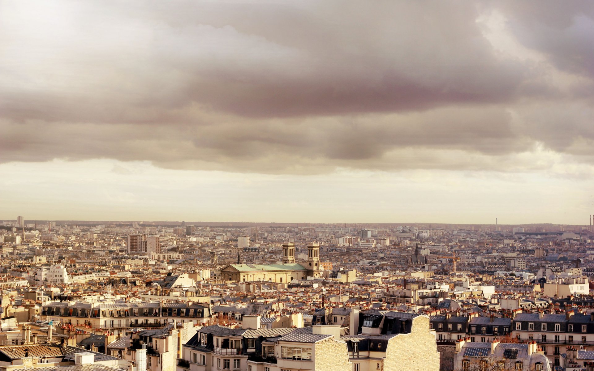 2K Quad HD PC desktop wallpaper/background of Paris cityscape: expansive man-made rooftops and monuments under moody clouds.