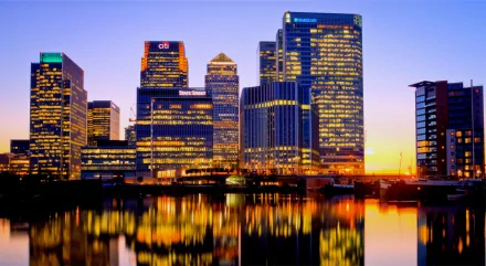 A stunning sunset over Canary Wharf, London, reflects beautifully off the Thames, showcasing illuminated skyscrapers in this man-made landscape.