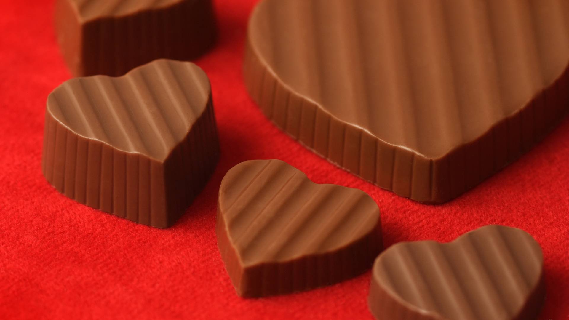 HD PC desktop wallpaper featuring close-up of heart-shaped and round chocolates on a red background, showcasing rich textures and smooth chocolate details.