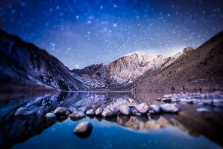 Tilt-shift nature scene, HD PC desktop wallpaper and background: miniature-style snowy mountain lake at dusk with starlit sky, foreground stones and mirror-like water reflection.