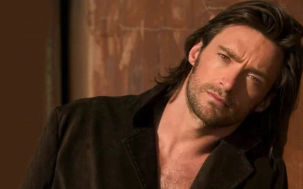 A striking HD desktop wallpaper featuring celebrity Hugh Jackman, showcasing his captivating gaze and layered hairstyle against a warm backdrop.