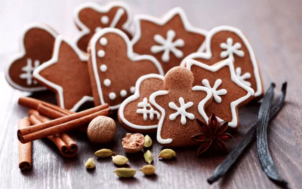 HD desktop wallpaper featuring decorated gingerbread cookies shaped like stars, hearts, and gingerbread men, surrounded by cinnamon sticks, vanilla pods, and spices.
