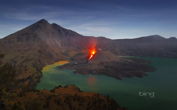 A stunning HD wallpaper capturing a volcano erupting with vibrant lava, surrounded by tranquil waters and mountainous terrain, showcasing the raw beauty of nature.