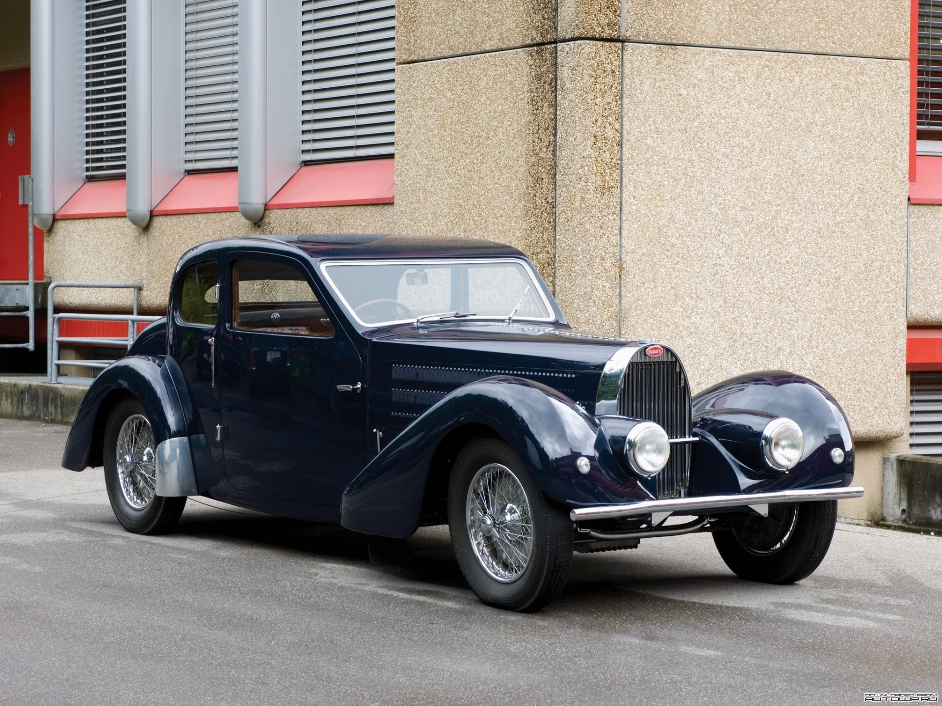 HD desktop wallpaper featuring a classic Bugatti Type 57 vehicle parked by a building, showcasing its vintage design and sleek dark blue exterior.