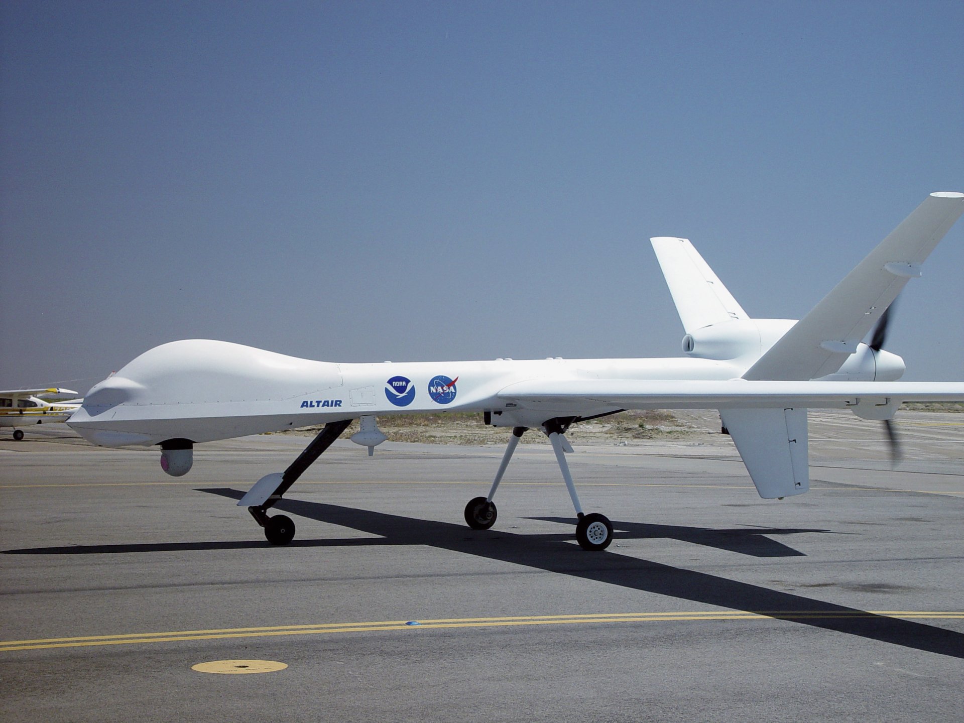 Military General Atomics MQ-1 Predator drone on a sunny tarmac, side profile under clear blue sky — 2K Quad HD PC desktop wallpaper background.