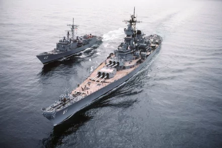 An aerial view of the USS Iowa (BB-61), a prominent battleship, accompanied by a smaller military vessel, showcasing naval power on the open sea as a striking HD desktop wallpaper.