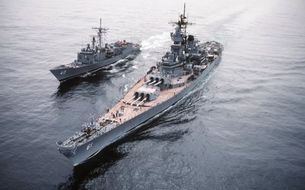 An aerial view of the USS Iowa (BB-61), a prominent battleship, accompanied by a smaller military vessel, showcasing naval power on the open sea as a striking HD desktop wallpaper.