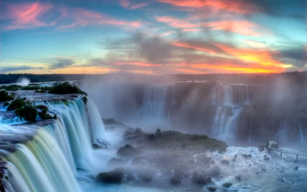 2K Quad HD PC desktop wallpaper/background: panoramic misty waterfall at sunset with multi-tiered cascades, glowing pink and blue sky, and churning river over rocky ledges.