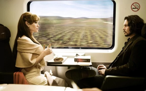 HD PC desktop wallpaper from the movie The Tourist: a woman in beige and a man in a dark coat sit facing each other in a train compartment, blurred fields passing by outside the window.