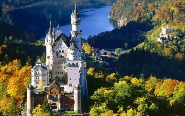 A stunning HD wallpaper of Neuschwanstein Castle, showcasing its intricate architecture surrounded by vibrant autumn foliage and a serene lake in the background.