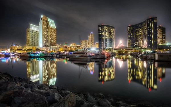 Nighttime view of the man-made San Diego skyline with illuminated buildings reflecting on calm harbor waters, captured in HD for a desktop wallpaper background.