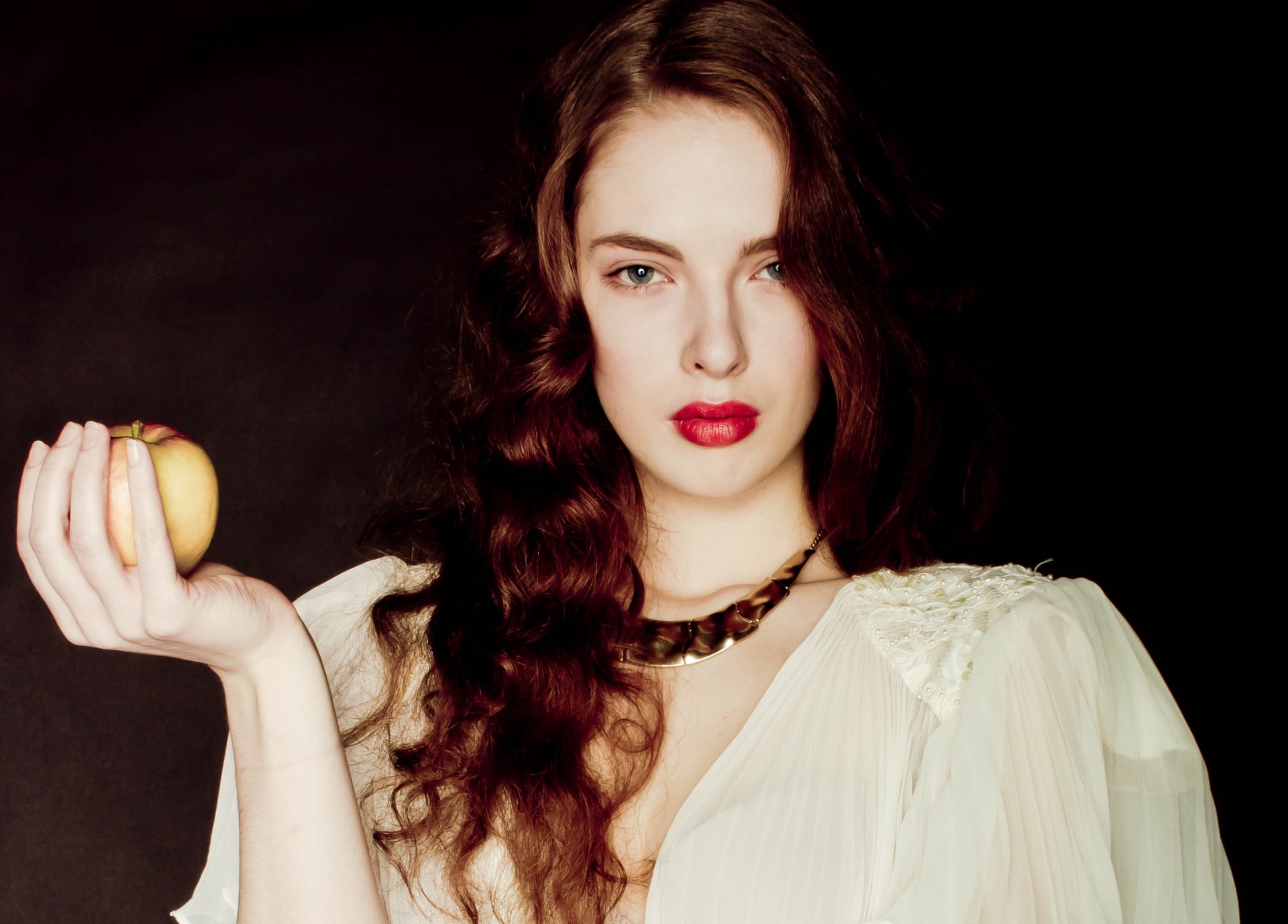 A striking HD desktop wallpaper featuring a beautiful woman with flowing hair, holding an apple, set against a dark background, exuding confidence and allure.