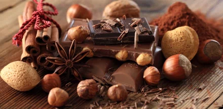 Rich chocolate bars surrounded by hazelnuts, cinnamon sticks, star anise, and cocoa powder, captured in stunning 4K Ultra HD for a mouthwatering PC desktop wallpaper.