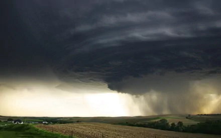 HD PC desktop wallpaper showing a dramatic tornado funnel descending from dark storm clouds over a rural landscape, capturing the raw power of nature.
