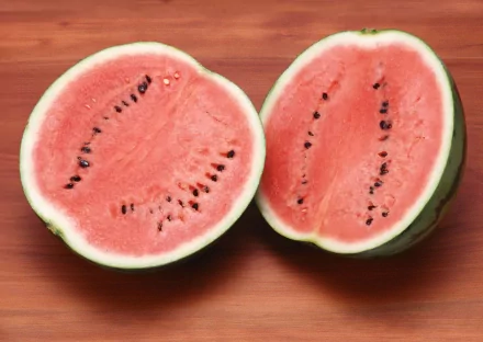 HD PC desktop wallpaper featuring a close-up of a ripe watermelon cut in half on a wooden surface, highlighting its juicy red flesh and black seeds.