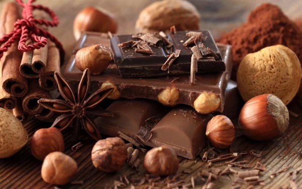 Rich chocolate bars surrounded by hazelnuts, cinnamon sticks, star anise, and cocoa powder, captured in stunning 4K Ultra HD for a mouthwatering PC desktop wallpaper.