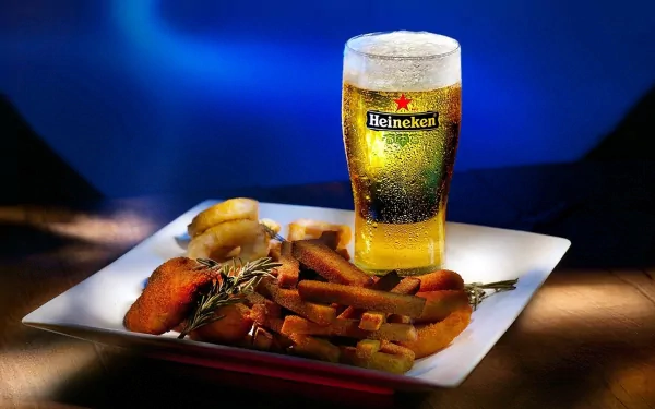 A vibrant HD desktop wallpaper featuring a pint of Heineken beer next to a plate of deliciously arranged food on a dark, blurred background.