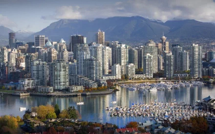 A stunning view of Vancouver, British Columbia, showcasing modern skyscrapers and a vibrant marina, set against the backdrop of mountains and a serene waterscape.