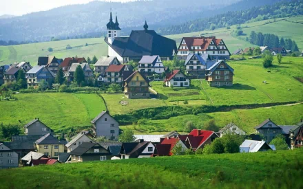 HD PC desktop wallpaper of a man-made village: rolling green hills dotted with traditional houses, a church steeple and colorful rooftops.