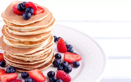 Stack of golden pancakes topped with strawberries and blueberries on a white plate, rendered as a 2K Quad HD PC desktop wallpaper/background.