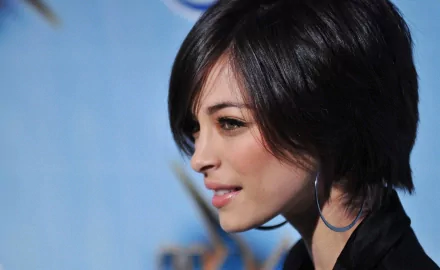 HD PC desktop wallpaper featuring a close-up side profile of celebrity Kristin Kreuk with short dark hair and a subtle smile against a blurred blue background.