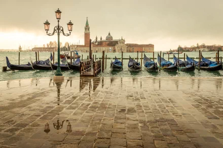 A stunning HD wallpaper of Venice, featuring gondolas moored along the waterfront, with a picturesque view of historic architecture reflected in the rain-soaked pavement.