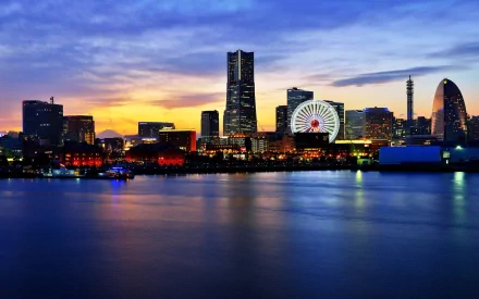 HD desktop wallpaper showcasing Yokohama's man-made skyline at sunset, featuring illuminated buildings and a ferris wheel reflected on calm waters.