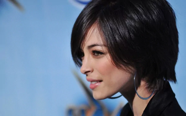 HD PC desktop wallpaper featuring a close-up side profile of celebrity Kristin Kreuk with short dark hair and a subtle smile against a blurred blue background.