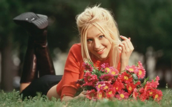 A vibrant HD wallpaper featuring Christina Aguilera, smiling and surrounded by colorful flowers, embodies the spirit of music and joy in a natural setting.