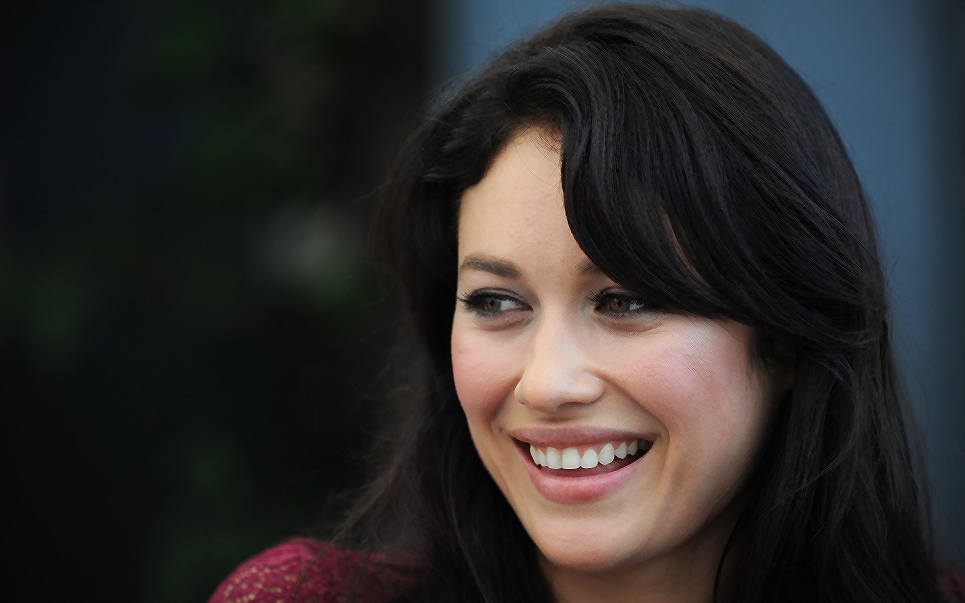 HD PC desktop wallpaper featuring a smiling Olga Kurylenko, the celebrity, with dark hair against a blurred dark background.