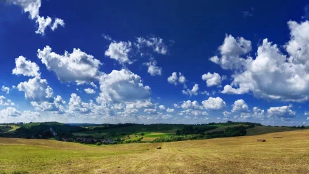 HD PC desktop wallpaper featuring a vast natural landscape with rolling hills under a bright blue sky dotted with fluffy white clouds.