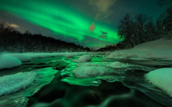 A mesmerizing display of the aurora borealis illuminates a snowy landscape, reflecting beautifully in a serene river, creating a stunning nature-inspired HD desktop background.