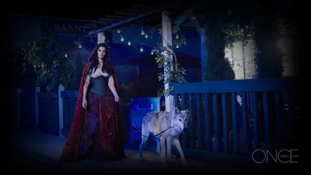 Red Riding Hood from Once Upon A Time walks with a wolf on a dimly lit path, exuding a mystical atmosphere. This HD wallpaper captures a captivating moment from the TV show.