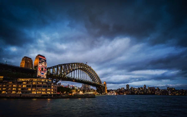 HD desktop wallpaper showcasing the Sydney Harbour Bridge under a dramatic evening sky, highlighting the iconic man-made structure against the cityscape.