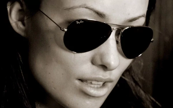HD PC desktop wallpaper: sepia close-up portrait of a woman in aviator sunglasses, intense gaze and slightly parted lips, high-contrast cinematic background.