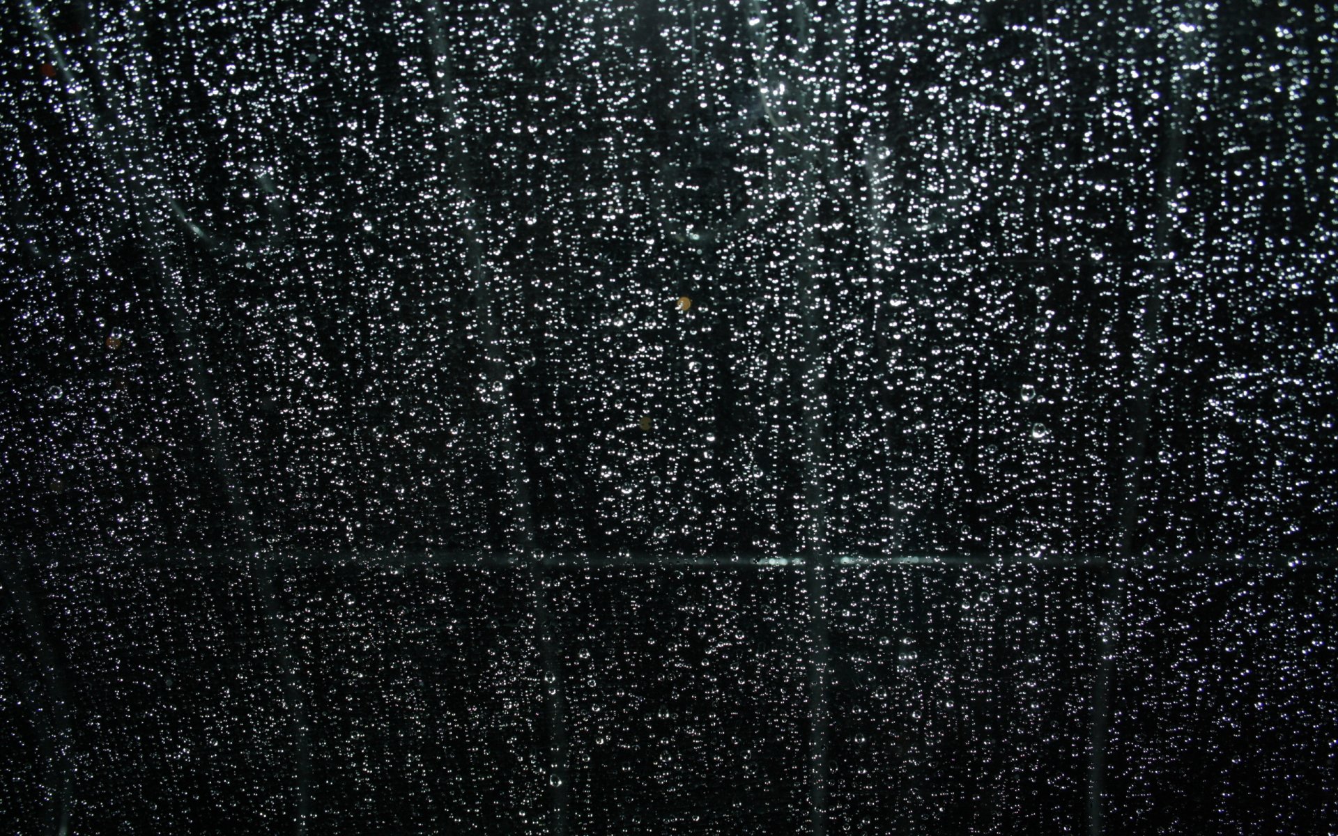 Close-up photography of raindrops on a dark window, glistening streaks and soft bokeh — 2K Quad HD PC Desktop Wallpaper and Background.