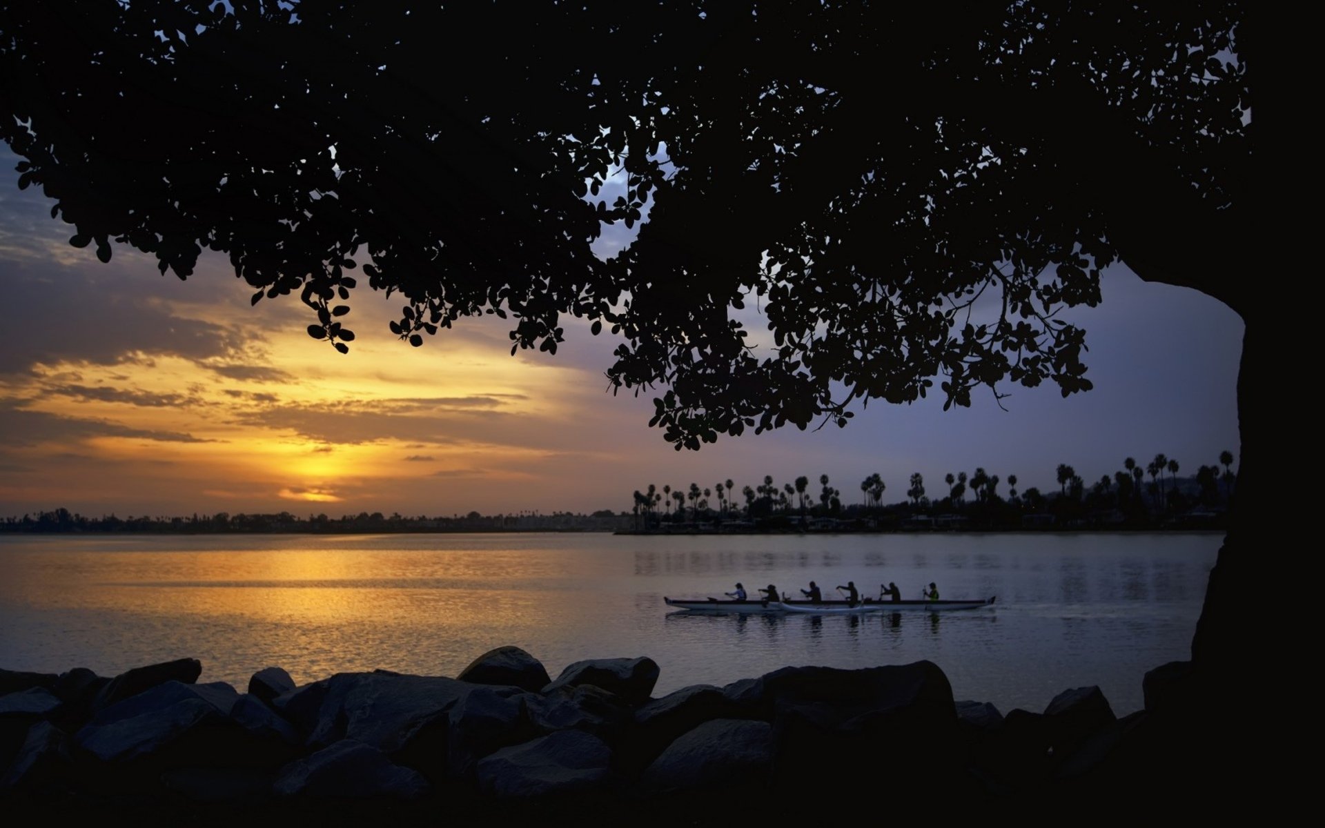 HD photography desktop wallpaper capturing a serene sunset over calm waters with silhouetted trees and rowers in a boat.