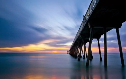 HD desktop wallpaper featuring a man-made pier extending over calm water at sunset with a dramatic sky.