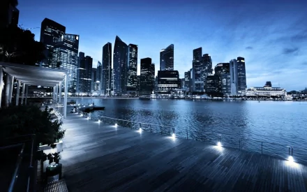 HD desktop wallpaper showing a man-made waterfront skyline of Singapore at dusk, with illuminated skyscrapers reflecting on calm water under a deep blue sky.
