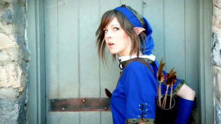 Lindsey Stirling in vibrant blue cosplay, resembling a fantasy character, stands against a rustic backdrop, capturing a dynamic and artistic moment. HD wallpaper and background.