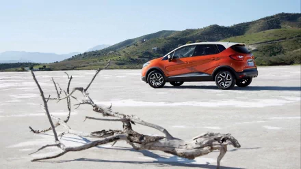 HD desktop wallpaper featuring an orange Renault Captur parked on a dry, cracked landscape with hills in the background.