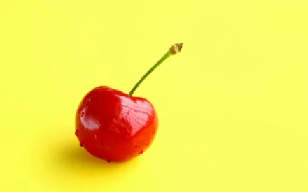 HD desktop wallpaper featuring a single glossy red cherry with a green stem on a bright yellow background, highlighting vibrant food imagery.