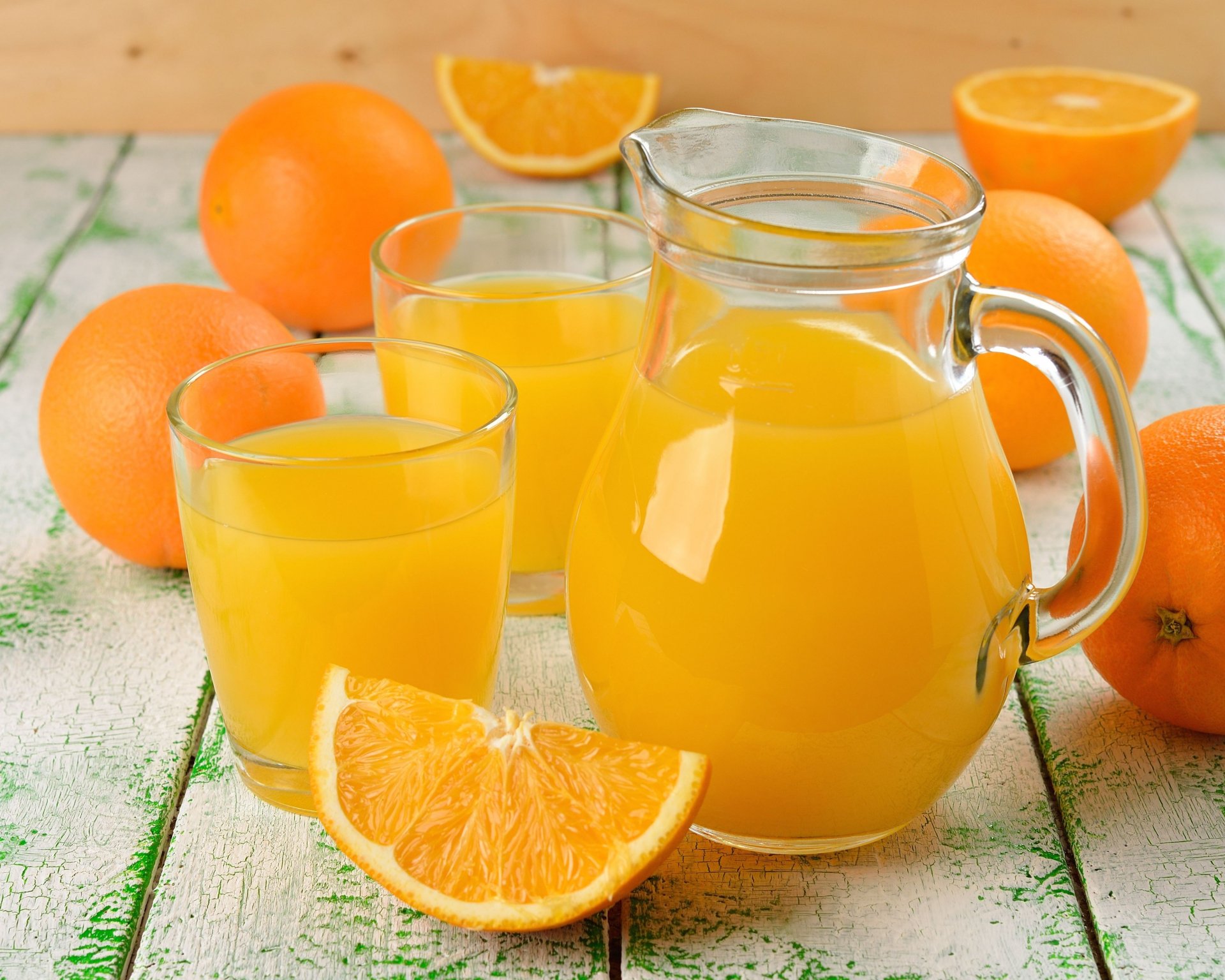 4K Ultra HD desktop wallpaper featuring a clear glass pitcher and two glasses filled with fresh orange juice surrounded by whole and sliced bright orange oranges.