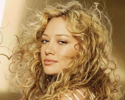HD wallpaper featuring celebrity Hilary Duff, showcasing her with beautiful curly hair and a soft, alluring expression against a warm background.