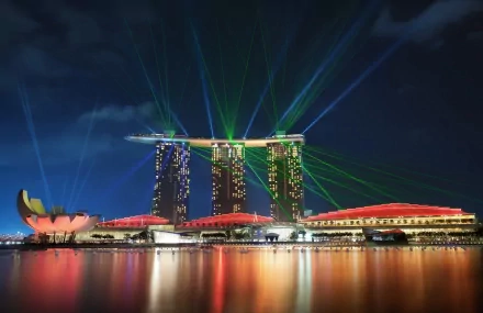 Nighttime view of Singapore's Marina Bay Sands with vibrant green laser lights illuminating the sky, reflected on calm waters in this HD desktop wallpaper.