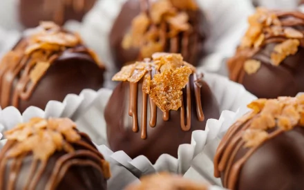 A close-up of delectable chocolate truffles topped with crispy flakes and drizzled with sweet chocolate, creating a rich and enticing food-themed desktop wallpaper.