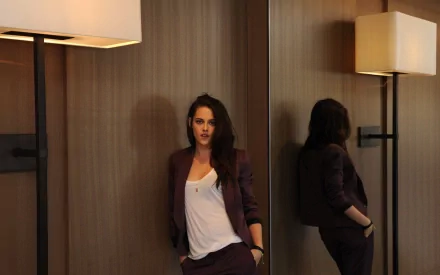 HD desktop wallpaper featuring American actress Kristen Stewart in a casual yet stylish outfit, leaning against a wooden wall, with a mirror and a floor lamp in the background.