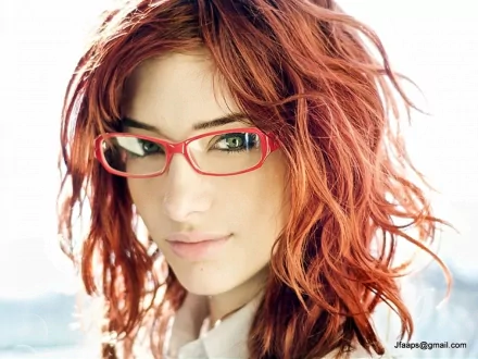 HD desktop wallpaper featuring celebrity Susan Coffey with red hair and red glasses against a bright, softly blurred background.